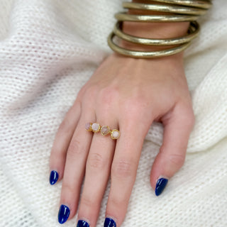 Hand wearing a gold ring with three stones on a white textured background