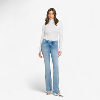 Woman wearing high rise light wash bootcut jeans with white long sleeve top and silver heels