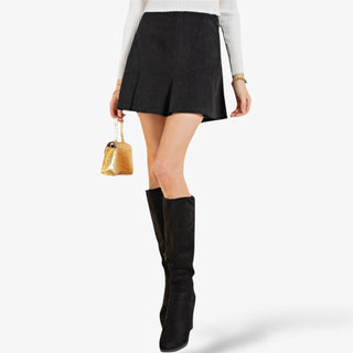 Black corduroy pleated mini skirt with a high waist and slight flare, styled with a white ribbed top and tall black boots for a chic fall outfit.