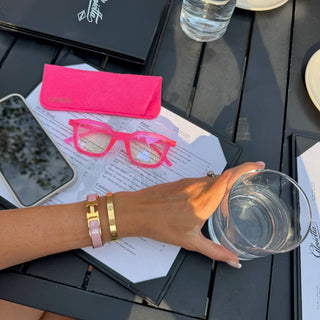 EyeJets Ibiza pink blue light reading glasses and matching case styled on a restaurant table with everyday accessories.