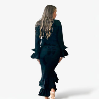 Woman wearing a black dress with ruffled sleeves and hem on a white background