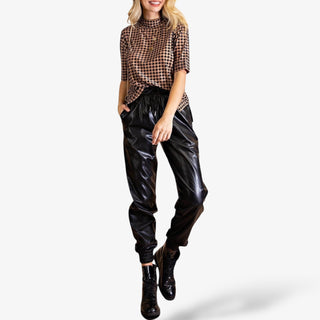 Black faux leather jogger pants with elastic waistband and cuffs, featuring a relaxed fit and shiny finish for a chic, edgy streetwear look.