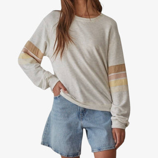 Person wearing a beige sweater with colorful stripes and denim shorts on a white background