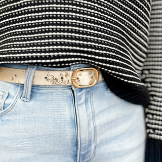Metallic gold distressed belt with a rounded gold buckle styled with light wash jeans and a black striped sweater for a chic and modern everyday look.