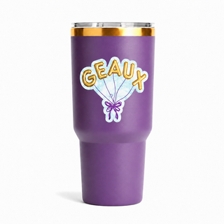 GEAUX vinyl sticker with gold balloon letters and a purple bow on a purple tumbler on a white background.