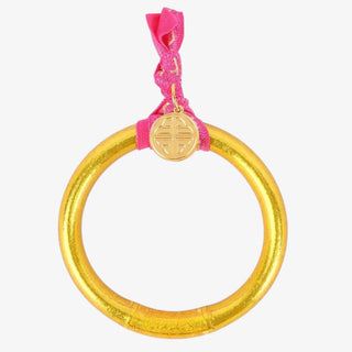 Gold bracelet with a pink hair tie and gold charm on a white background