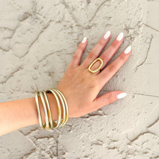 Gold oval statement ring on hand with polished open design styled with silver and gold bangle bracelets close-up view