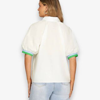 Woman wearing a white blouse with green trim on a plain background