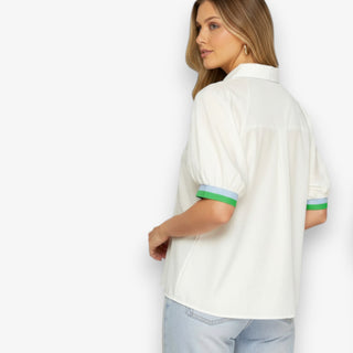 Woman wearing a white shirt with green and blue trim on a plain background