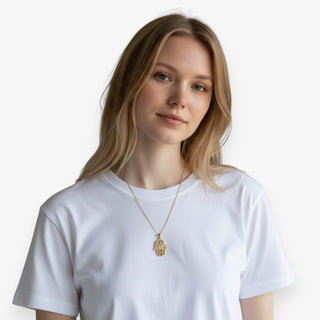 Woman wearing a white t-shirt and gold chain necklace with a hamsa hand pendant against a plain background