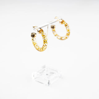 Hoo Hoops Gold Glitter Mini Hoop Earrings in clear acrylic shown from an angled side view on a display stand.