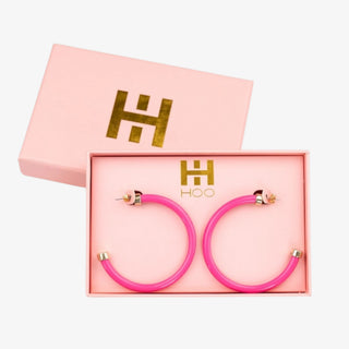 Bright pink acrylic hoop earrings with gold-tone accents on white background
