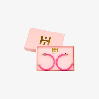 Bright pink acrylic hoop earrings with gold-tone accents on white background

