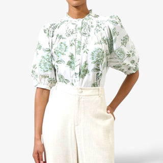 Person wearing a floral blouse and white pants on a white background