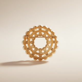 Gold brooch with intricate design on a beige background