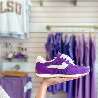 Dolce Vita B. Noticed GameDay Purple sneaker held in front of a clothing rack with purple garments.