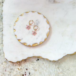 Pair of gold and pink star-shaped earrings on a white stone surface