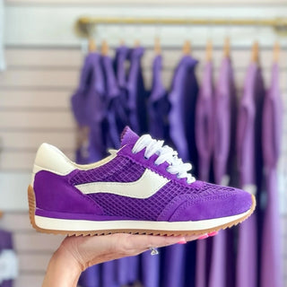 Dolce Vita B. Noticed GameDay Purple sneaker held in front of a clothing rack with purple garments.