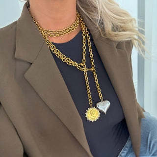 Model wearing a chunky gold chain necklace with a large silver heart pendant, styled with a blazer.