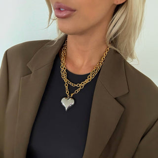 Model wearing a chunky gold chain necklace with a large silver heart pendant, styled with a blazer.