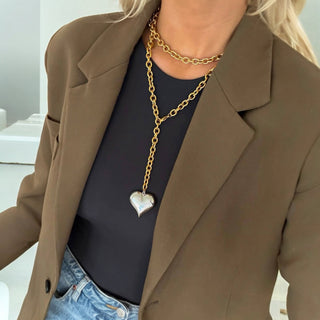 Model wearing a chunky gold chain necklace with a large silver heart pendant, styled with a blazer.