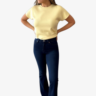Person wearing a yellow short sleeve top and dark blue jeans on a white background
