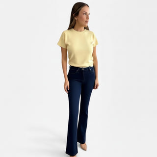 Woman wearing a yellow top and dark blue jeans on a white background