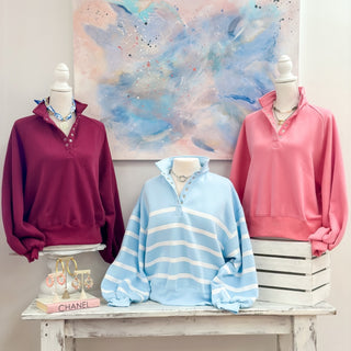 Three mannequins wearing colorful sweatshirts against a decorative wall.