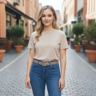 Woman in beige shirt and blue jeans standing on a street with plants and buildings in the background