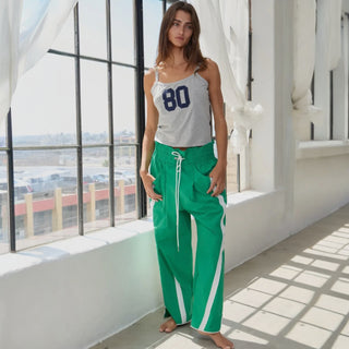 Woman wearing a gray tank top with the number 80 and green pants with white stripes indoors.