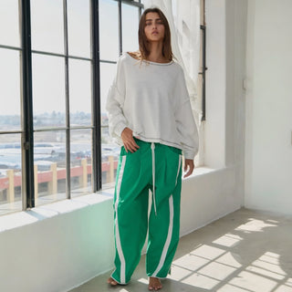 Woman wearing a white sweater and green pants with white stripes indoors.