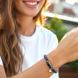 Woman wearing a blue Dharma beaded bracelet with a Budha charm, smiling outdoors.