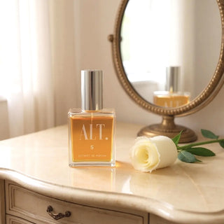 Perfume bottle labeled 'ALT.' on a marble surface with a rose and mirror in the background.