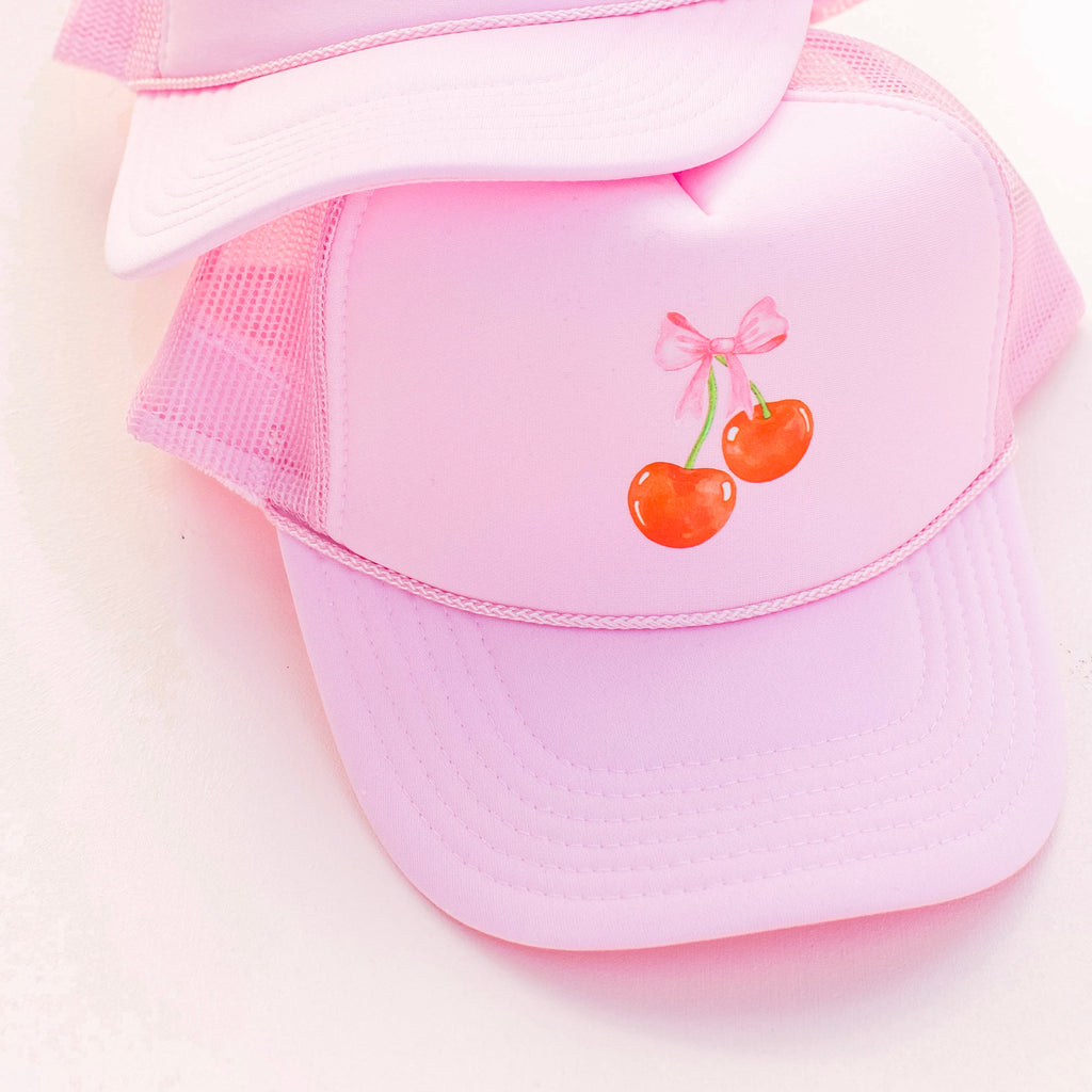 Our Space 46 Bow and Cherries Trucker Hat in Pink is on trend and stylish for Spring 2024. This hat features a pink bow and red cherries with an adjustable tab for fit. Printed in the USA.