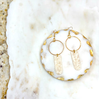 Gold hoop earrings with white stone accents on a marble surface