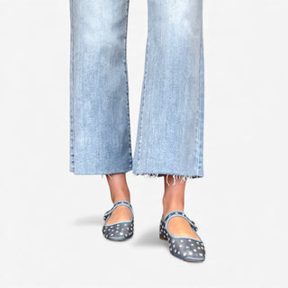 Woman wearing blue mary jane flats with rhinestone detailing and jeans on a grey background.