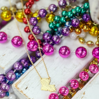 Colorful Mardi Gras beads with a gold Louisiana necklace on a white surface