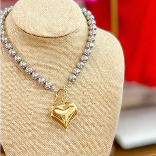 Necklace with a gold heart pendant on a beige stand against a red background