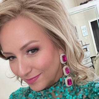 Woman wearing a teal embellished top and pink earrings indoors.