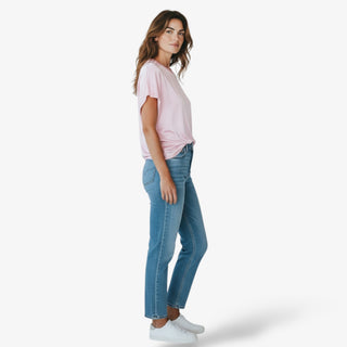 Woman wearing a blush pink short sleeve t-shirt and blue jeans on a white background