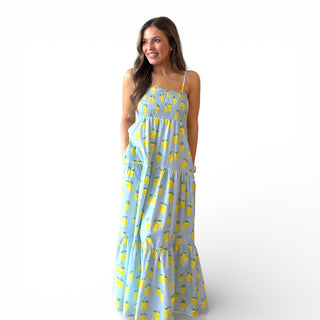 Blue lemon print maxi dress with smocked bodice, adjustable spaghetti straps, and tiered skirt on a smiling model against a clean background.