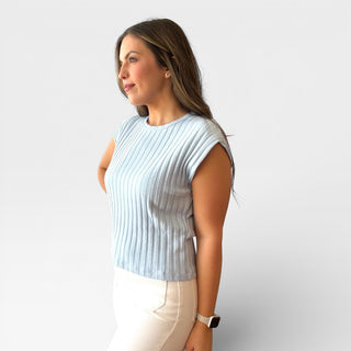 Woman wearing a light blue sleeveless ribbed top against a white background