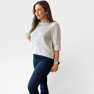 Woman wearing a metallic silver sweater and blue jeans on a white background