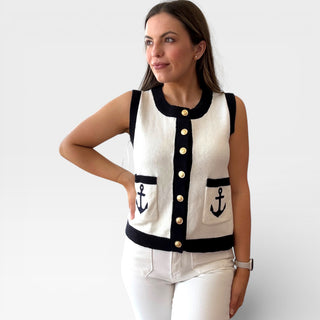 Woman wearing a white sleeveless sweater with black accents and anchor designs on a plain background