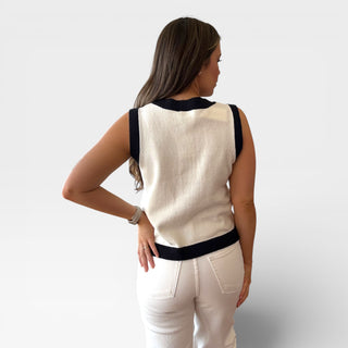 Back view of a woman wearing a beige sleeveless top with black trim on a plain background