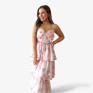 Pink floral tiered midi dress with pleated bow bodice, spaghetti straps, and layered ruffle skirt shown on model, perfect for Easter, spring events, and garden parties.