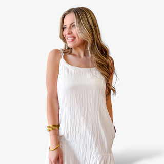 White sleeveless mini dress with button strap detail, lightweight crinkle fabric, relaxed fit, and flowy hem for an effortless spring and summer outfit.