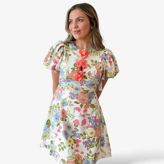 Floral print mini dress with multicolor flowers, short puff sleeves, fitted waist, and statement 3D floral appliqué neckline for a feminine spring and Easter outfit.