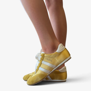 Model wearing the J Slides Peggy Sneaker in a suede and silk yellow and white. 