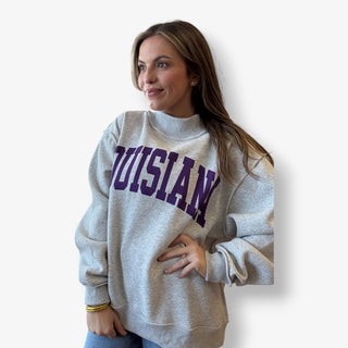 Woman wearing a gray sweatshirt with 'Louisiana' printed in purple on a white background